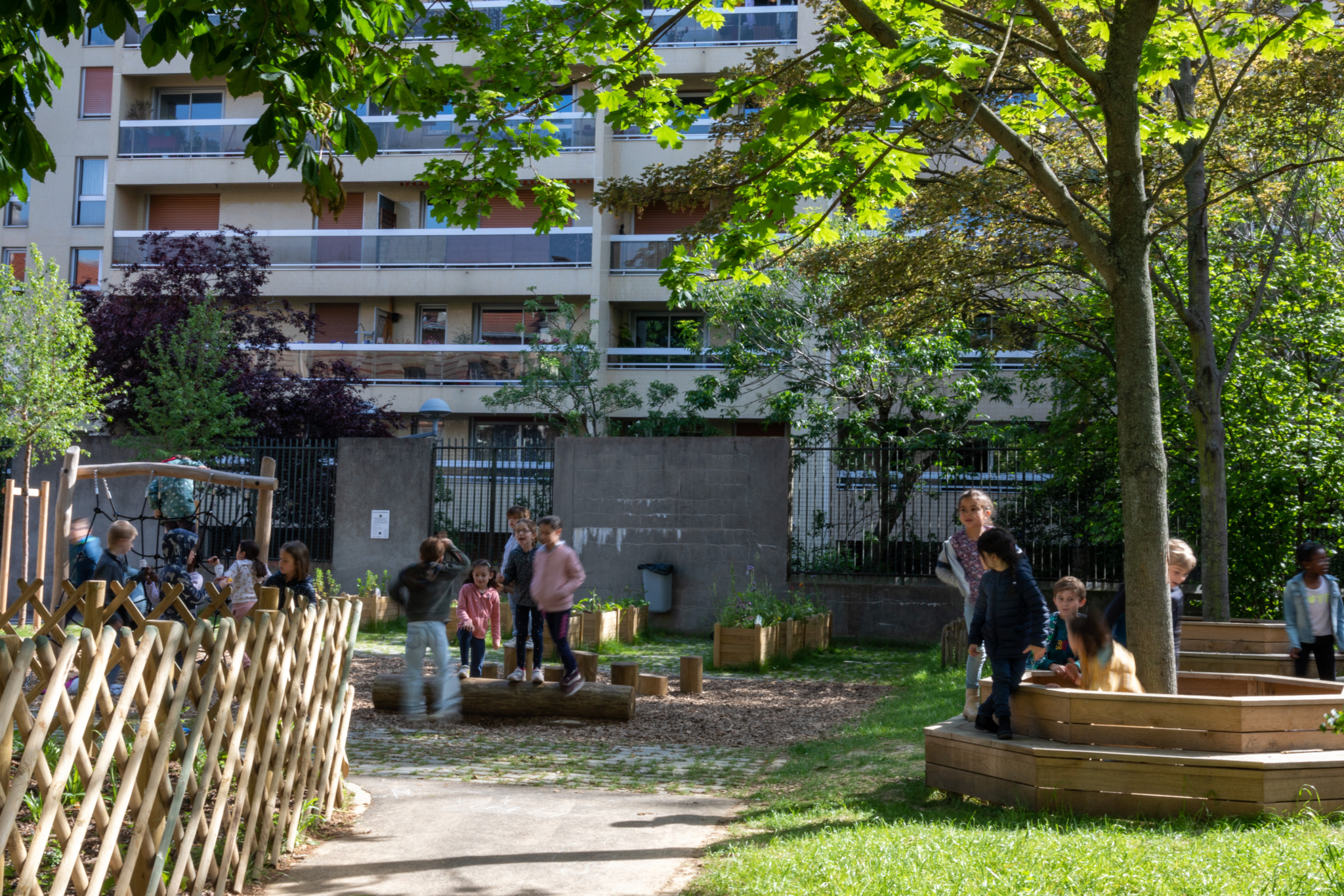 Des grumes et des bancs en tour d'arbre permettent aux enfants de profiter de l'ombre des arbres existants. 