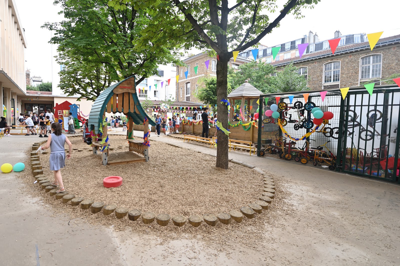 Cour de maternelle - Cabane en bois dans la zone de copeaux centrale et asphalte en périphérie pour la circulation des vélos