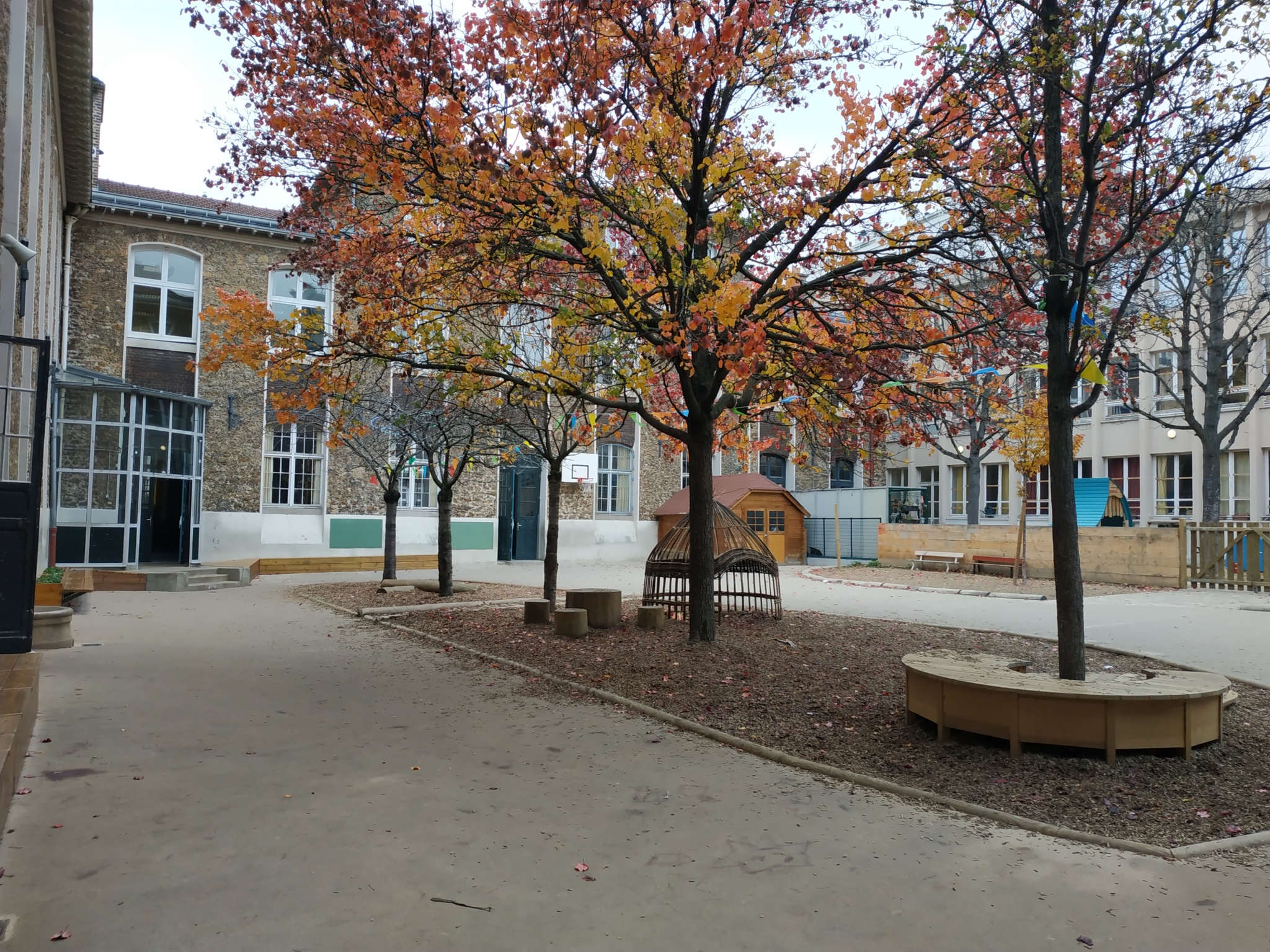 Cour 1 de l'élémentaire - zone perméable centrale avec assises, cabane et grumes au pied des fruitiers