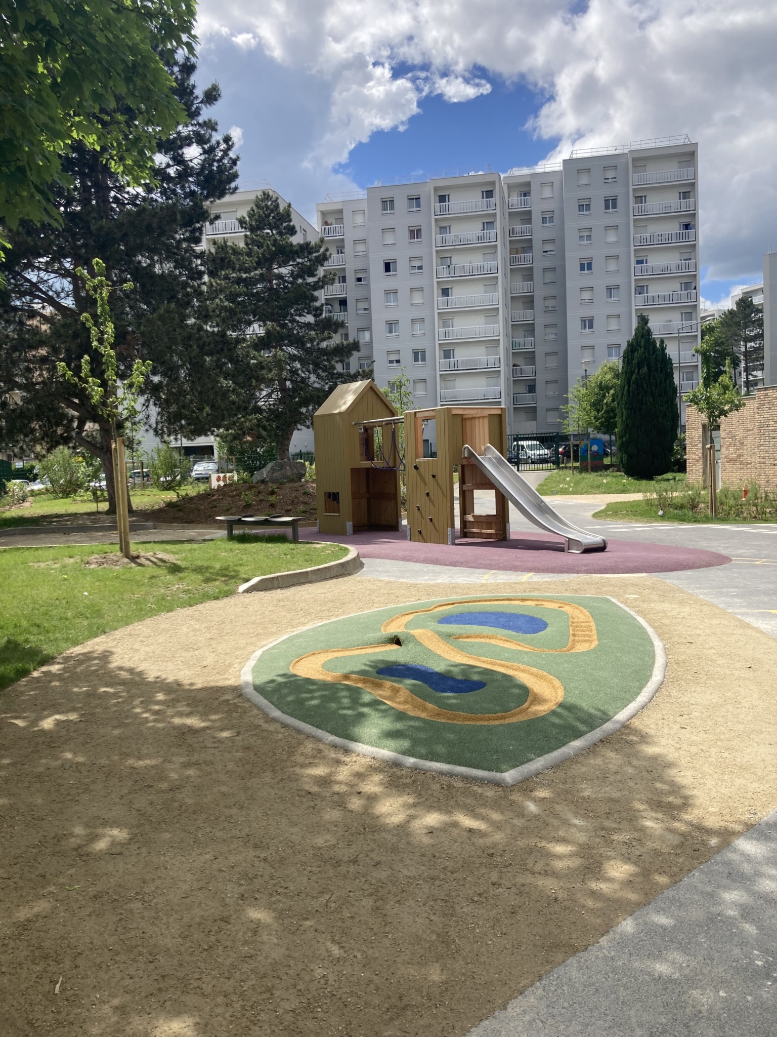 En premier plan, le parcours de bille ; à l'arrière, une structure de jeux avec toboggan, pont suspendu et cloches pour faire de la musique. | 